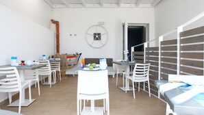A dining area with white chairs and tables, a clock on the wall, and a wooden fence in the background.