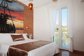 A bedroom with a large bed, a wooden accent wall, a painting of a ship, and a view through a glass door. - Rivazzurra Design Rooms (San Vito Lo Capo)