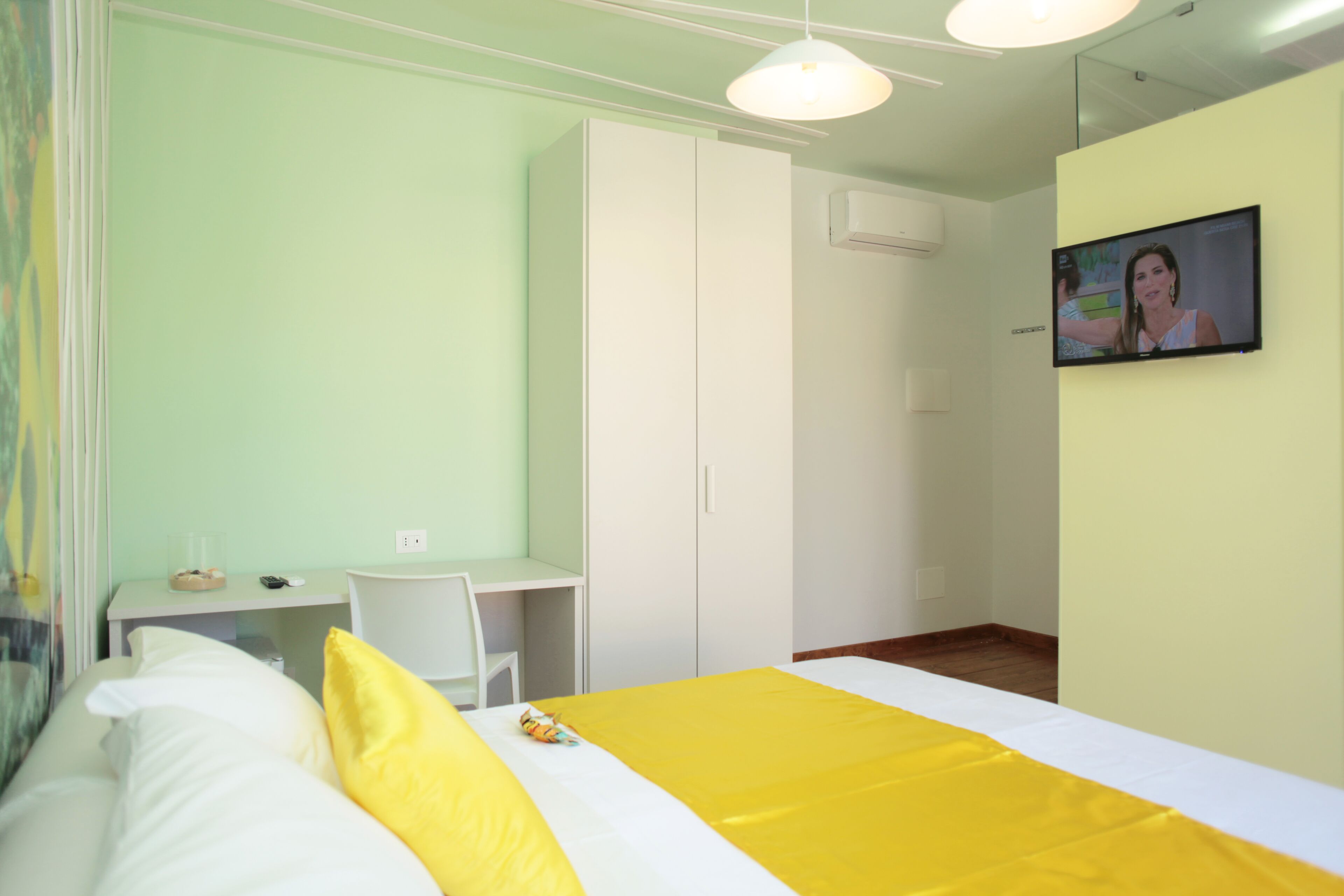 Camera d'albergo con un letto, una scrivania, un armadio e una televisione a parete.