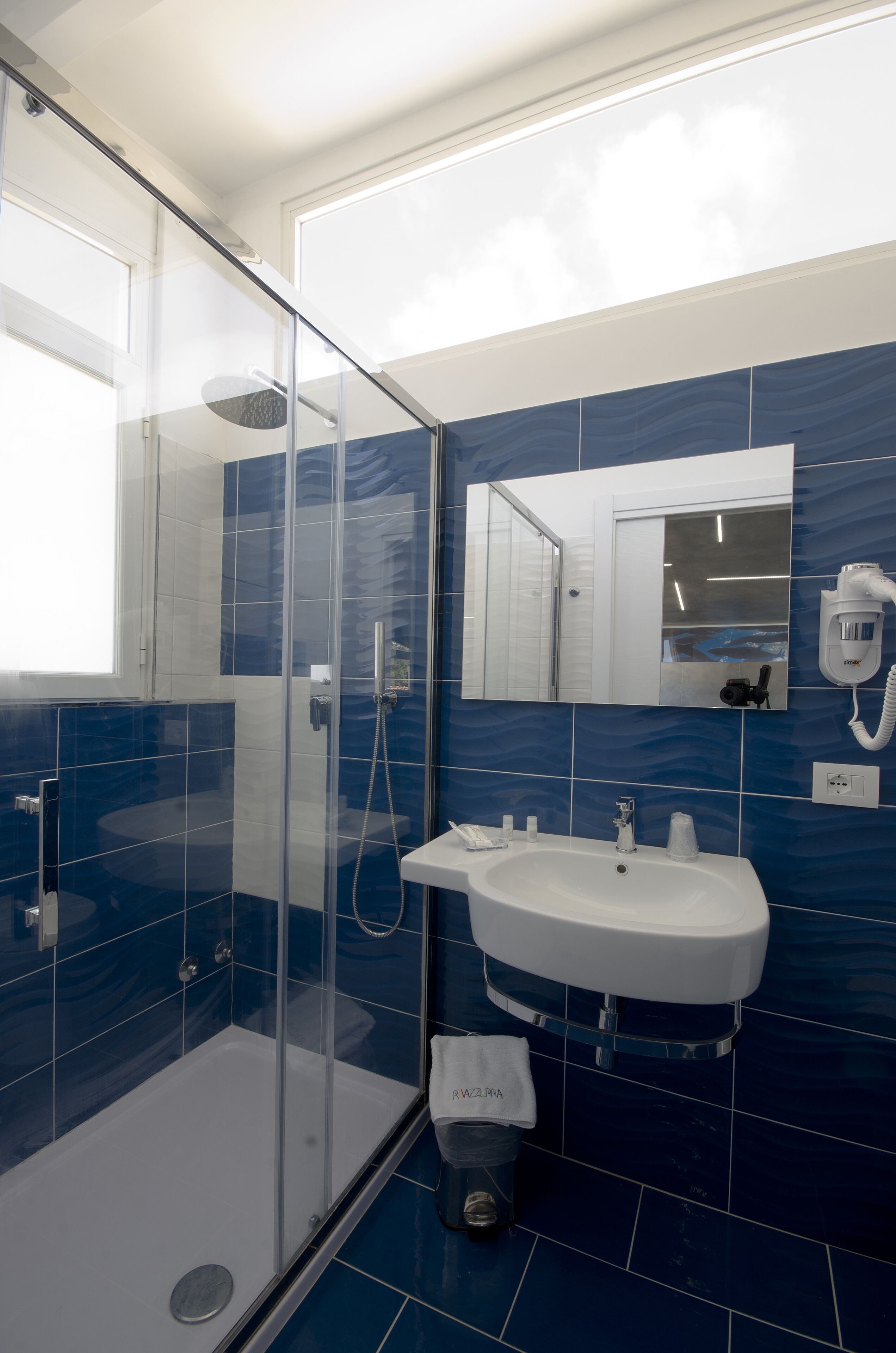 A modern bathroom with a glass shower enclosure, a white sink, and a mirror.