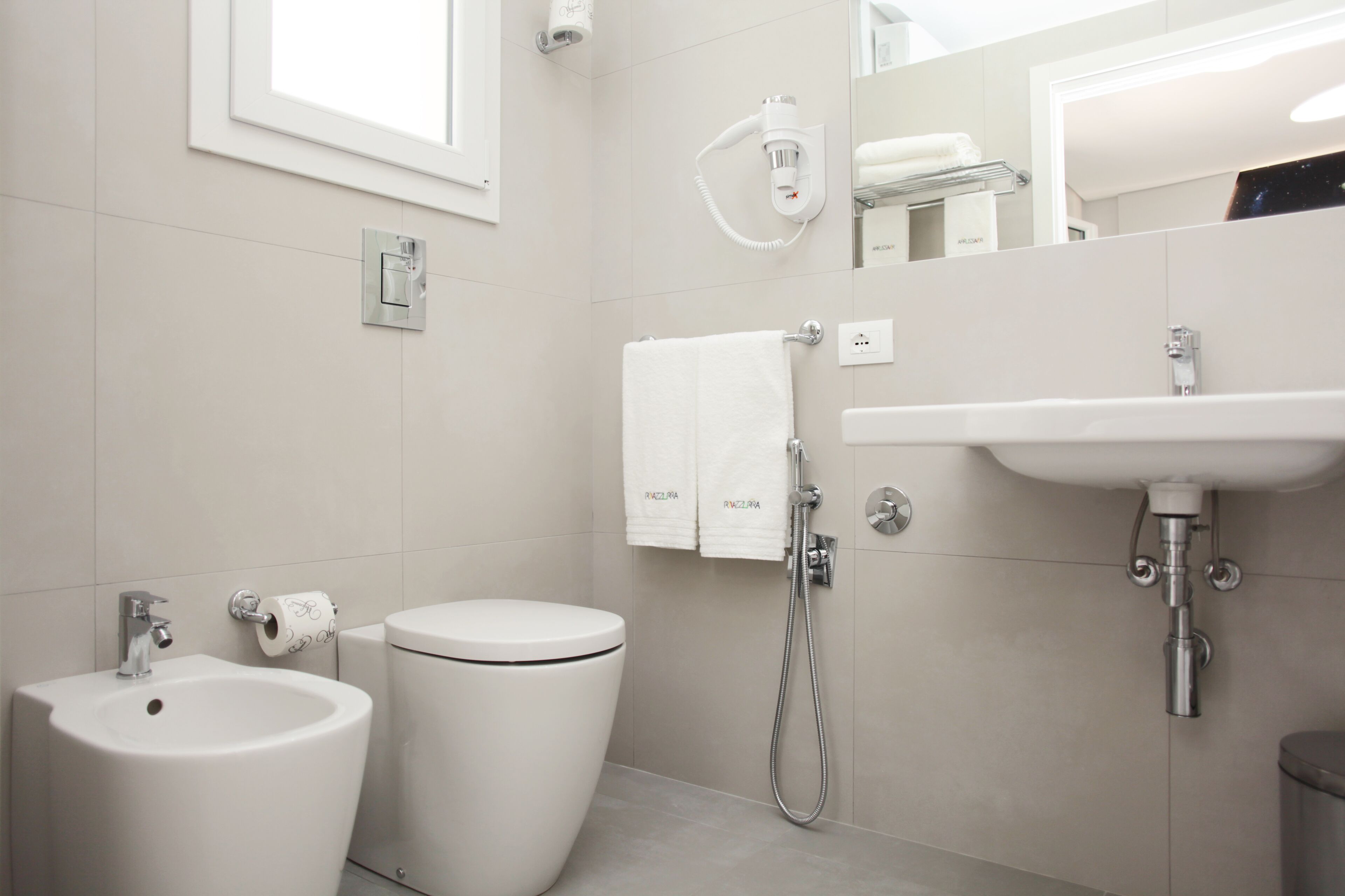 A modern bathroom with a bidet, toilet, sink, and towel rack.