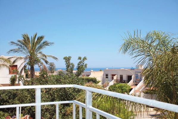 A coastal view with a white railing, palm trees, and buildings with a clear sky. - Rivazzurra Design Rooms (San Vito Lo Capo)
