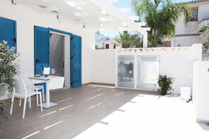 A bright room with a white table and chairs, a blue door, and a window overlooking a mountain. - Rivazzurra Design Rooms (San Vito Lo Capo)
