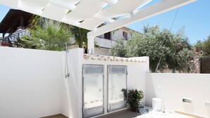 A covered outdoor area with a white wall, a metal gate, and a potted plant.