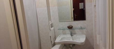 A bathroom with a glass shelf, a white sink, a towel rack, and a shower area.