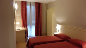 Una habitación de hotel con dos camas, un escritorio con lámpara, una silla y una puerta.