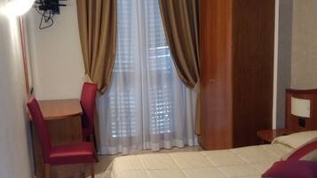 Ein Hotelzimmer mit einem Bett, einem Schreibtisch mit Stuhl, einem Fernseher und Vorhängen.