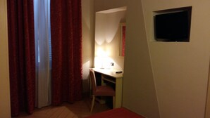 Una habitación pequeña con luz tenue, que tiene un escritorio, una silla y un televisor colgado en la pared.