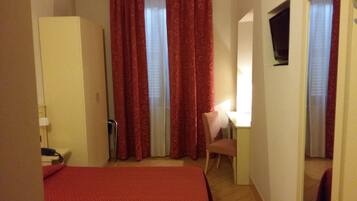 A hotel room with a bed, a desk, a chair, and a TV.