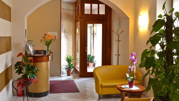 Un área de recepción con un mostrador de madera, un sofá amarillo, plantas en macetas y un perchero.