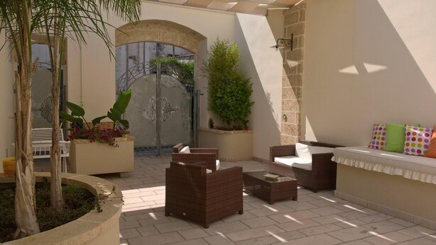 Un patio iluminado por el sol con muebles de mimbre, un banco blanco y plantas en macetas.