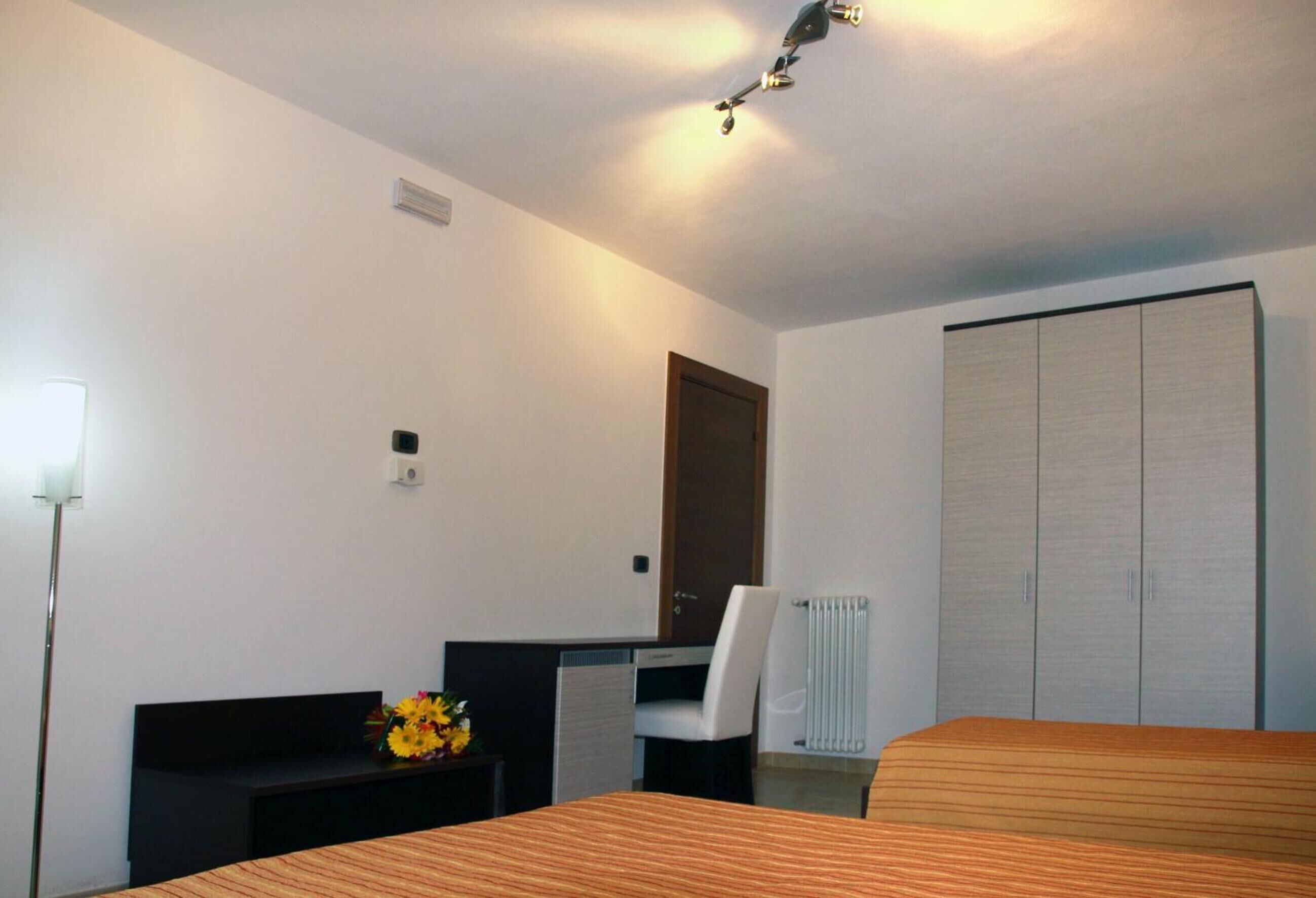 A hotel room with a bed, a desk, a chair, a wardrobe, and a radiator.