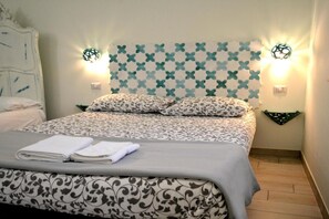Quarto de hotel com cama, roupa de cama estampada, luminárias fixadas na parede e cabeceira decorativa.