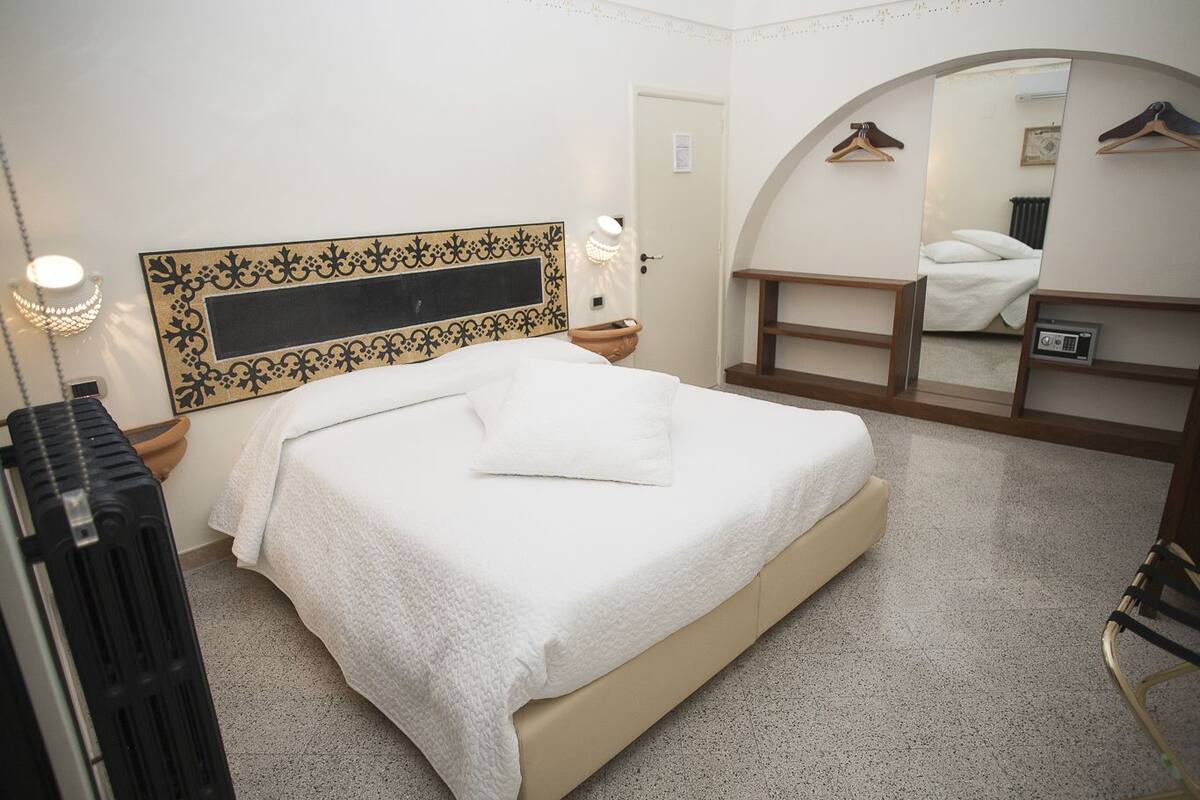 Siististi järjestetty hotellihuone, jossa on sänky, peili, patteri ja vaatekaappi.