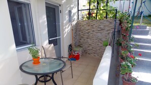 A small patio with a round glass table and two chairs, surrounded by potted plants and a stone wall. - Nikos Apartments (Sithonia)