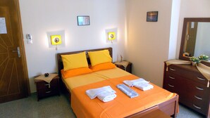 A neatly arranged hotel room with a bed, bedside tables, a dresser, and an air conditioning unit on the wall. - Nikos Apartments (Sithonia)
