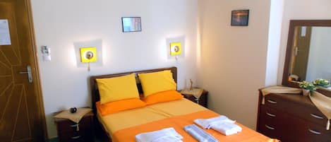 A neatly arranged hotel room with a bed, bedside tables, a dresser, and an air conditioning unit on the wall.
