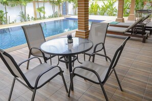 A poolside area with a round table and chairs, a tiled floor, and a pool with a blue border.