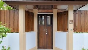 A double wooden door with a number '10' above it, flanked by beige walls and a concrete step leading to the entrance. - CAPITAL O887 Orchid Garden Villa 2 (Rawai)