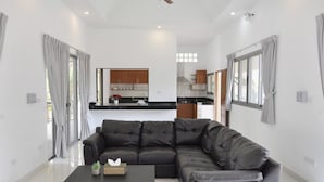 A modern living room with a sectional sofa, a coffee table, and a kitchen in the background. - CAPITAL O887 Orchid Garden Villa 2 (Rawai)