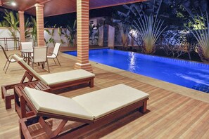 Ett område vid poolen med trädäck och solstolar samt en pool.