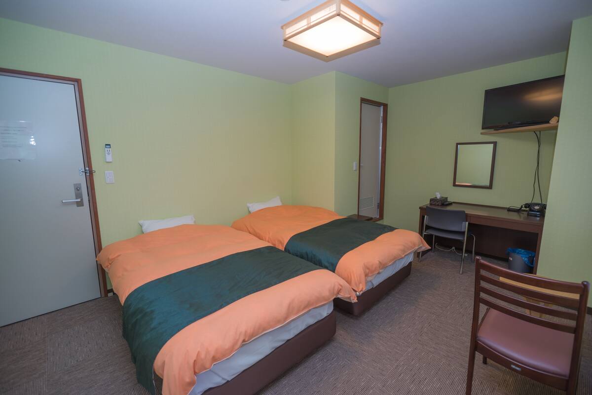 Une chambre avec deux lits, un bureau, une chaise, une télévision et une porte.