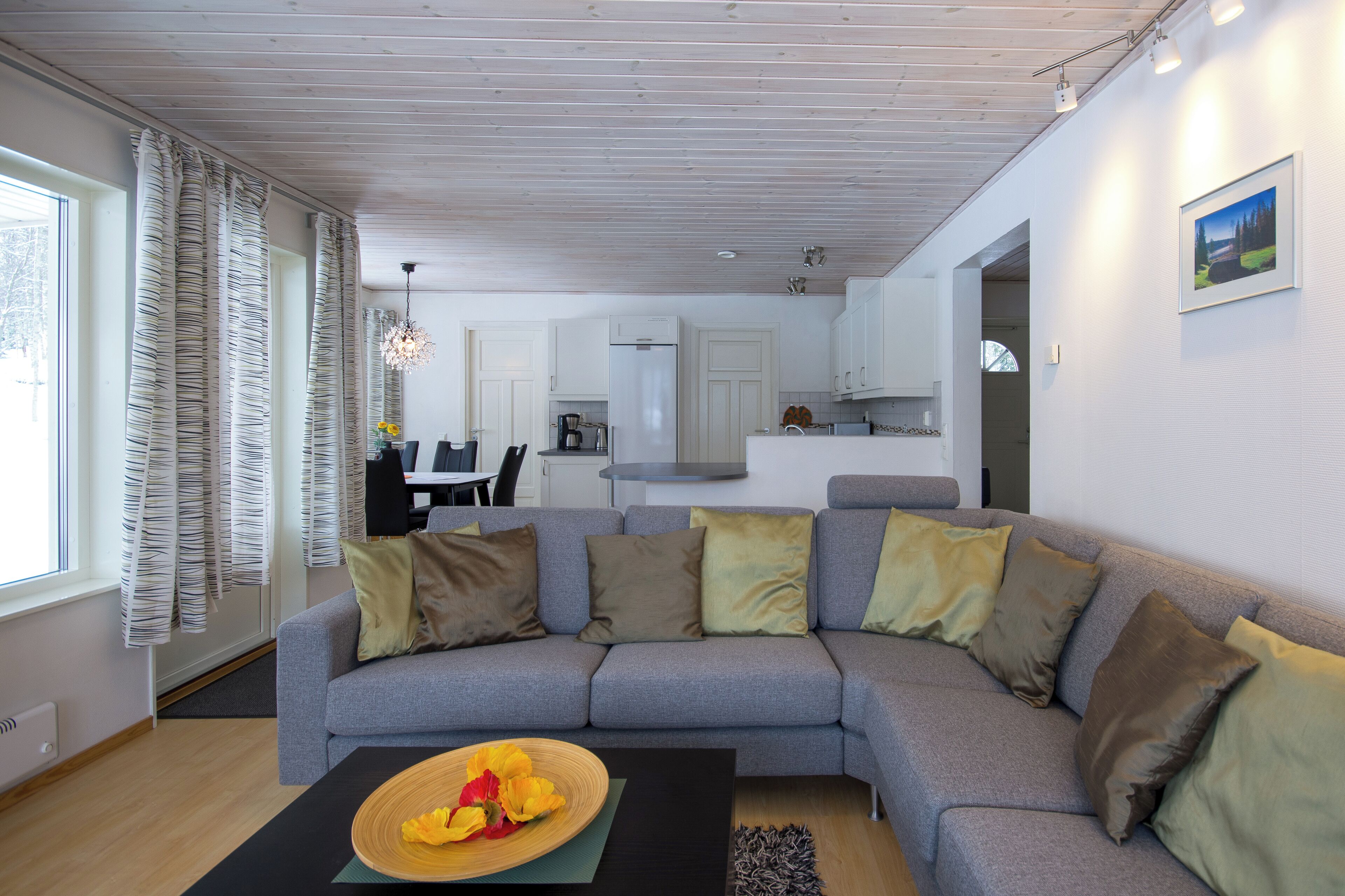 A modern living room with a grey sectional sofa, a coffee table with a bowl of fruit, and a dining area in the background.