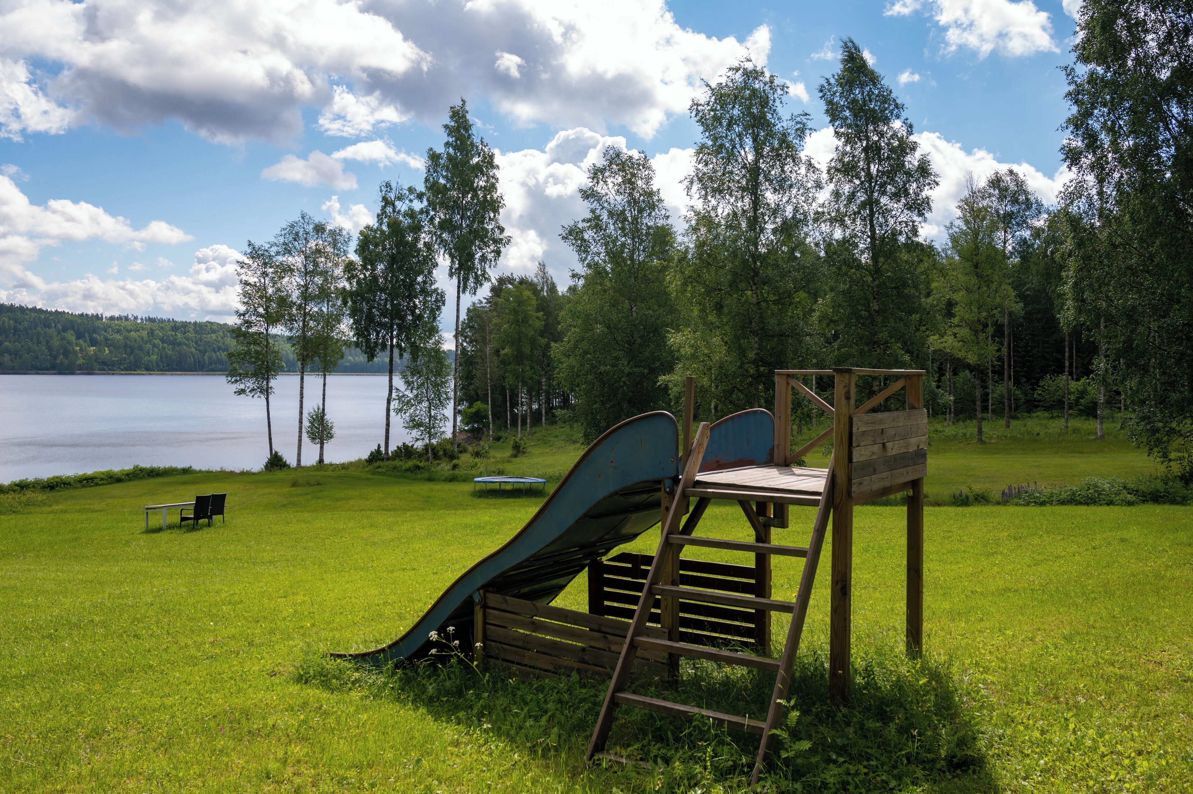 A playground with a slide and a bench near a lake surrounded by trees.