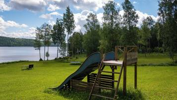 A playground with a slide and a bench near a lake surrounded by trees.