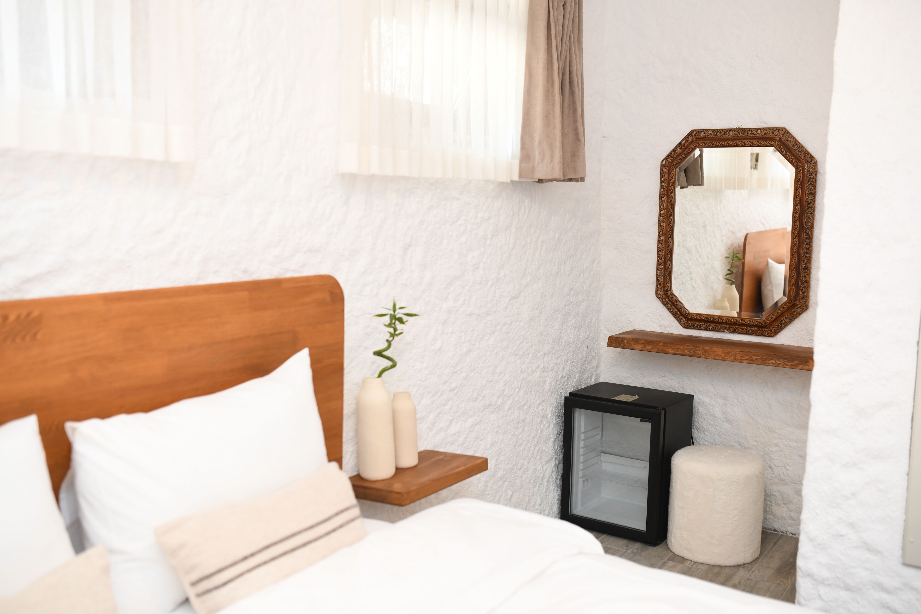 Un dormitorio con cabecera de madera, una mesita de noche con velas, un espejo y un pequeño armario negro.
