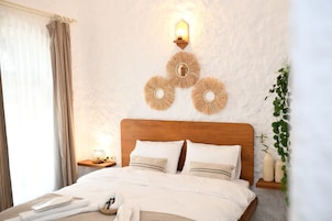 Una cama bien hecha con ropa blanca, un cabecero de madera y una mesita de noche con una lámpara.