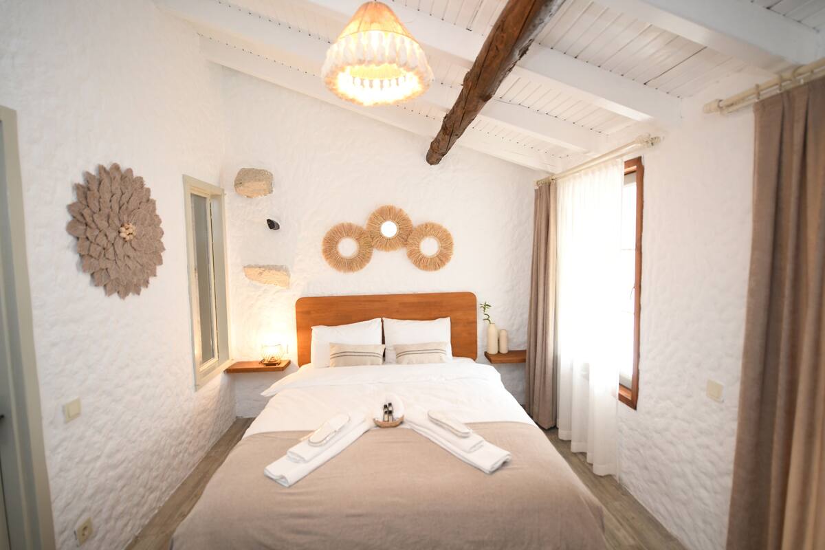 A hotel room with a wooden headboard, a large bed with white linens, a chandelier, and a decorative wall piece.