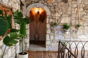 Un interior de paredes de piedra, piso de madera, un arco rústico y plantas colgantes.