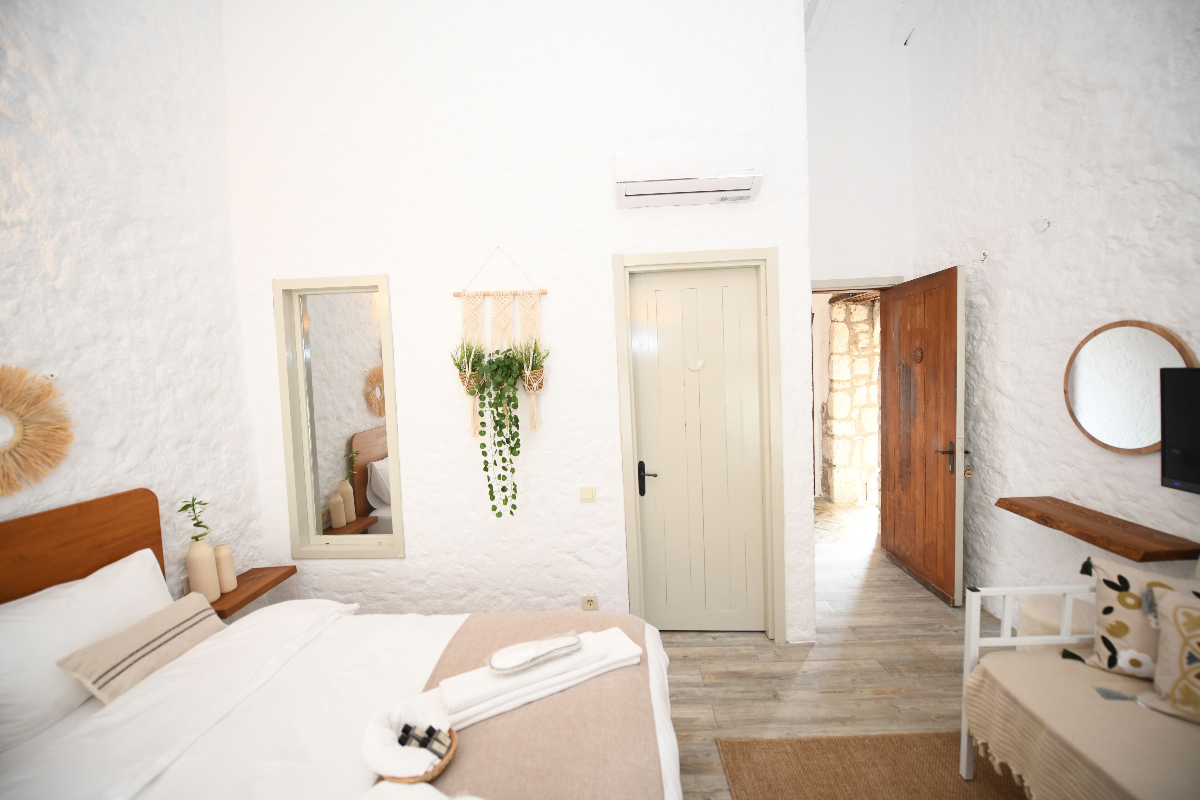 Quarto com cama, mesa de cabeceira, espelho, plantas pendentes e televisão.