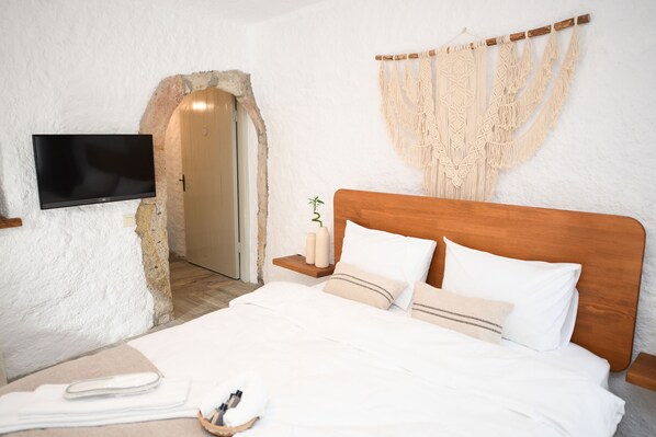 A bedroom with a wooden headboard, a flat-screen TV mounted on the wall, a macrame wall hanging, and a small bedside table with a plant. - MAHZEN ALACATI BUTIK OTEL (Cesme)