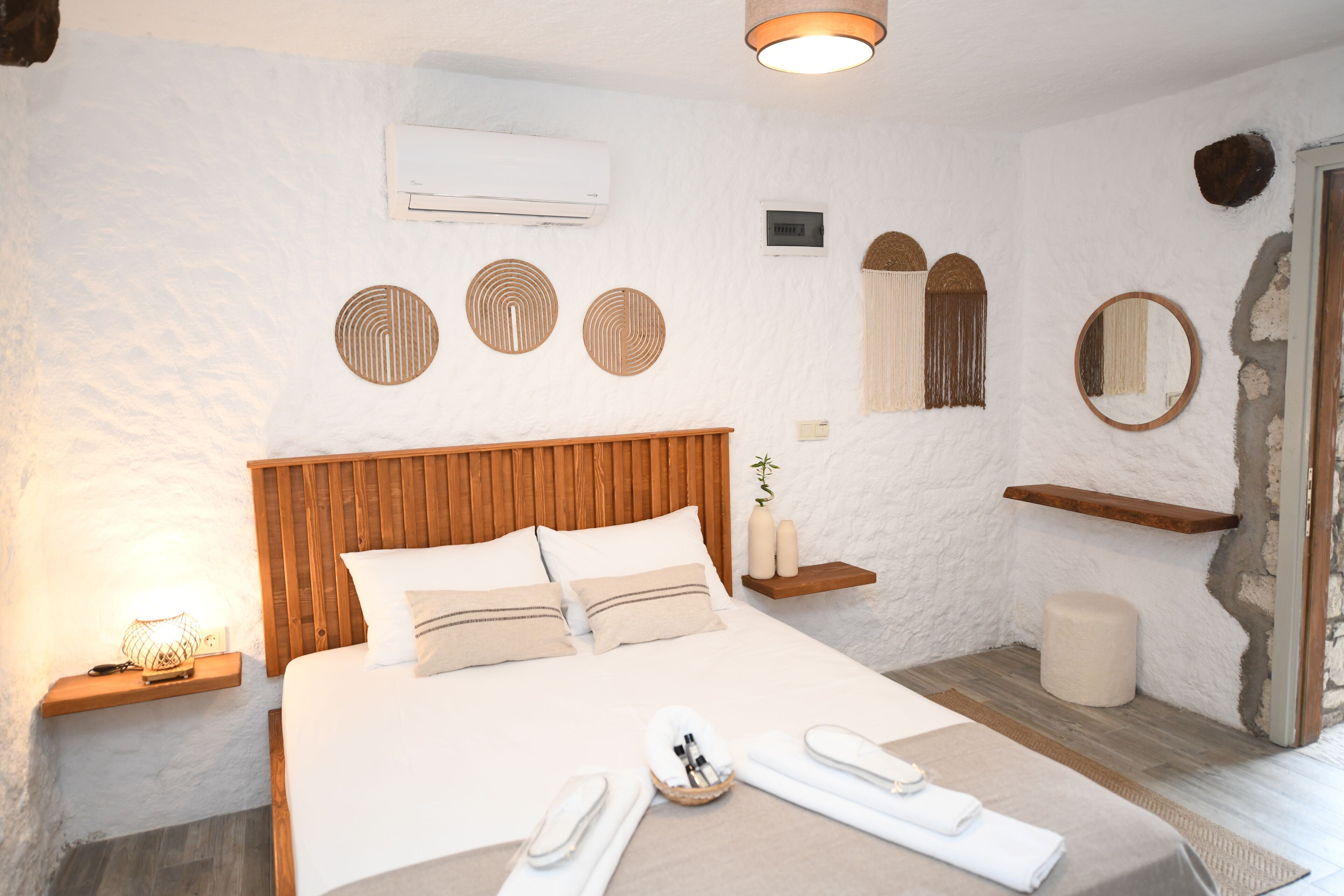 Una camera da letto con testiera in legno, un letto con lenzuola bianche, un comodino con una lampada e un condizionatore d'aria a muro.