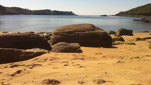 A sandy beach with large rocks in the foreground and calm water in the background. - Authentic mill with feet in water (near the sea) (Le Vieux-Marché)