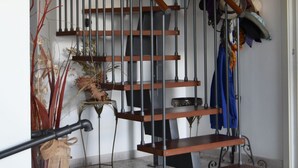 A spiral staircase with wooden steps and metal railings, leading to a landing area with a coat rack and a vase of dried plants. - Country House Erba Regina (Frascati)