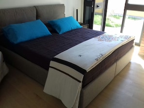 A bed with a dark headboard, two blue pillows, and a white bedspread with a floral design.