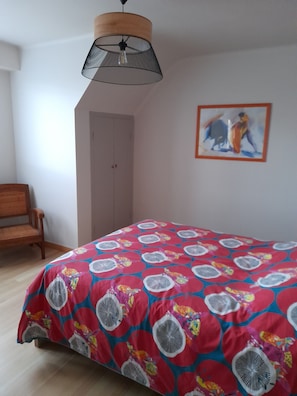 A bedroom with a bed, a chair, a door, and a painting on the wall.