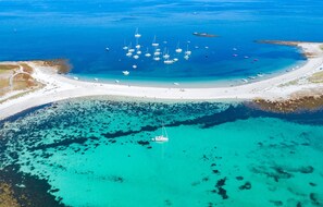 An aerial view of a coastal area with a beach, clear turquoise waters, and numerous boats anchored near the shore.