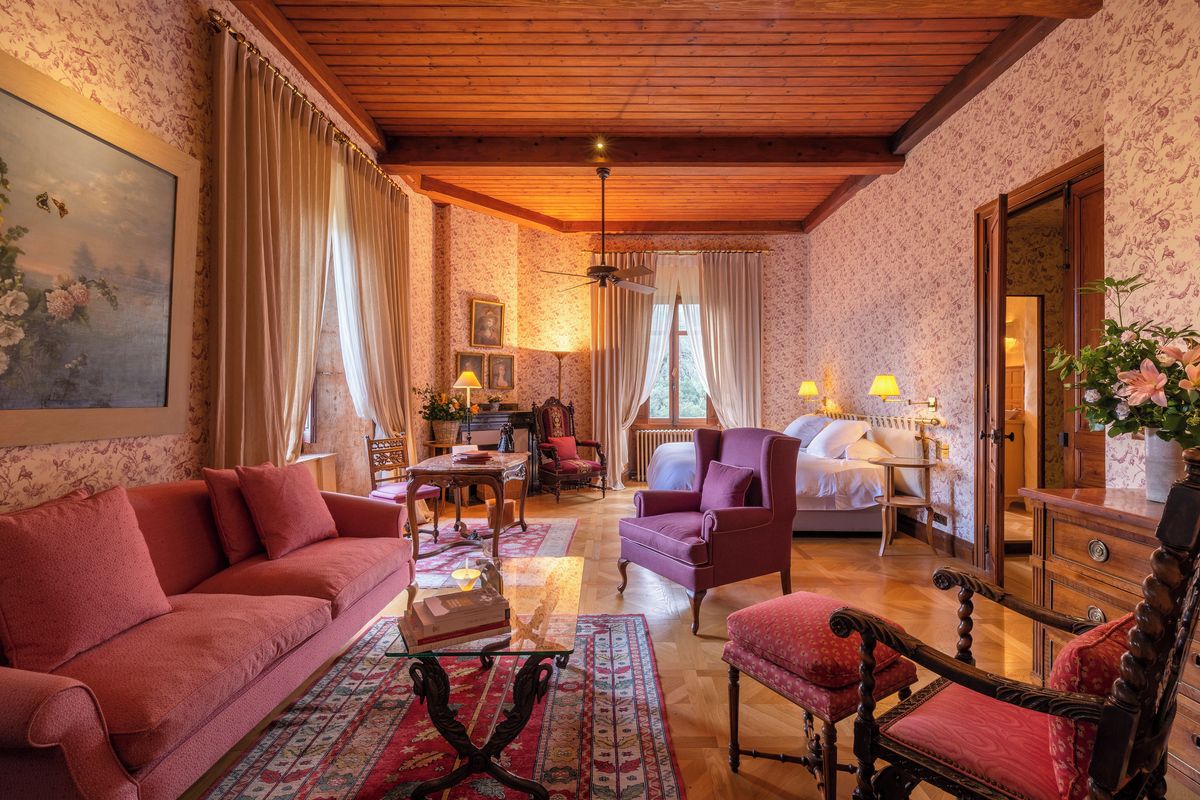Une pièce chaleureuse avec un plafond en bois, un canapé, un fauteuil, un lit et une table avec une lampe.