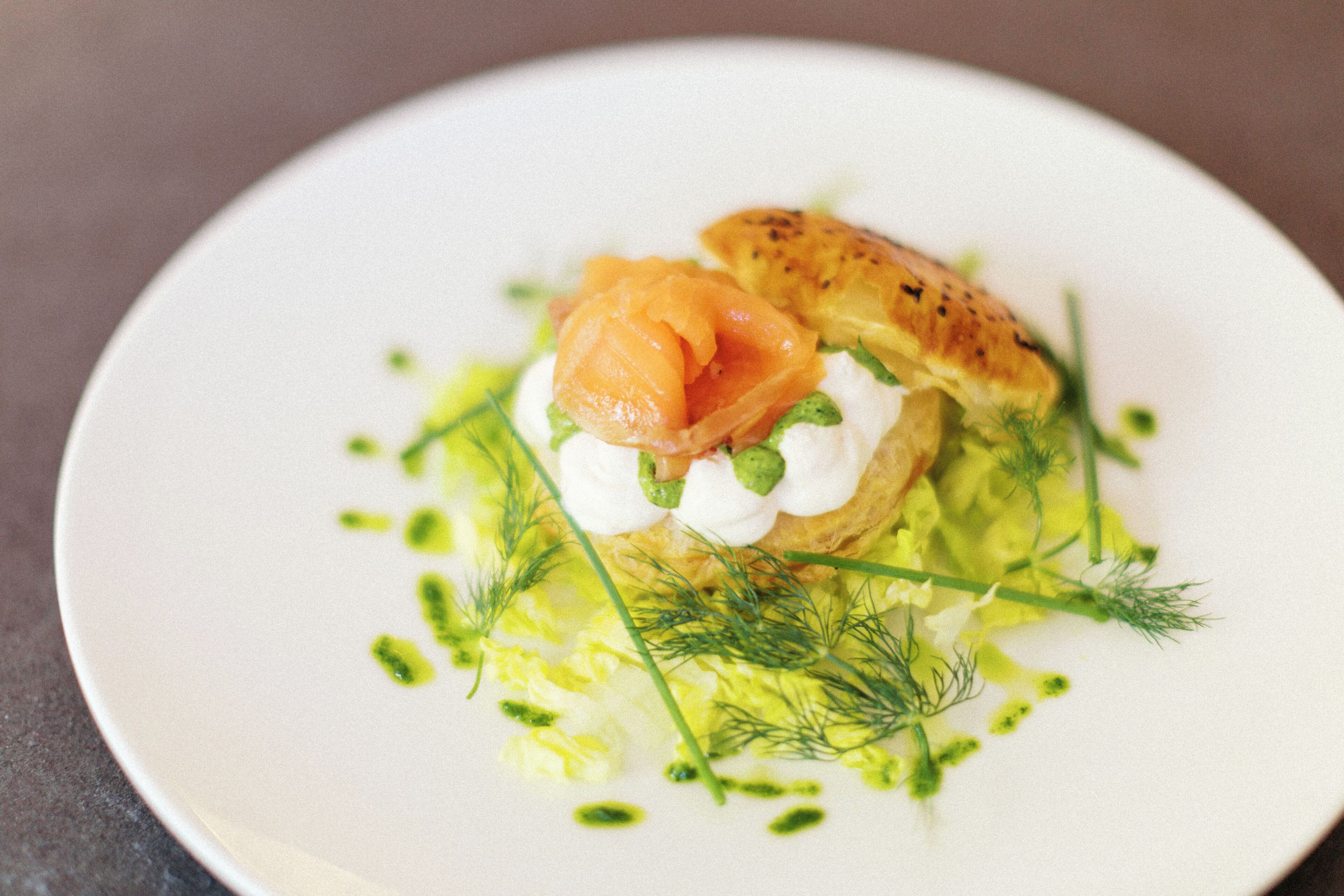 A plate with a pastry, salmon, cream, and green garnish.
