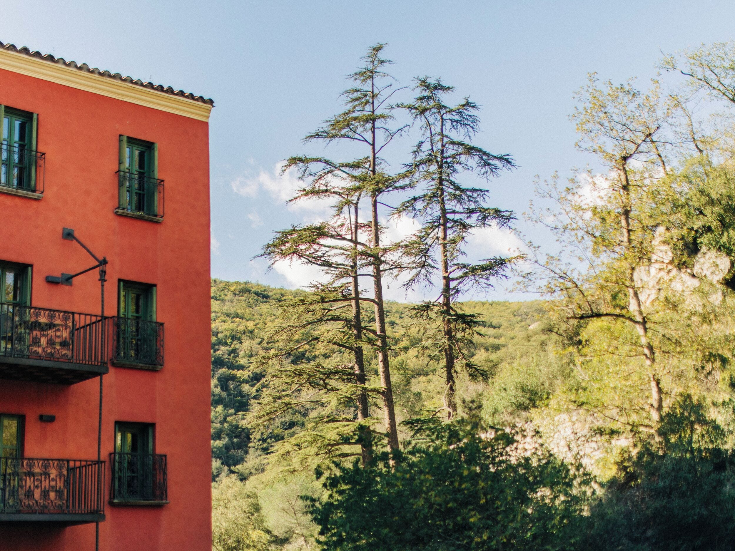 A red building with balconies and a forested hillside in the background.