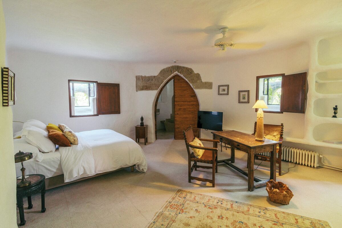 A bedroom with a bed, a desk, a chair, a lamp, a radiator, and a window.