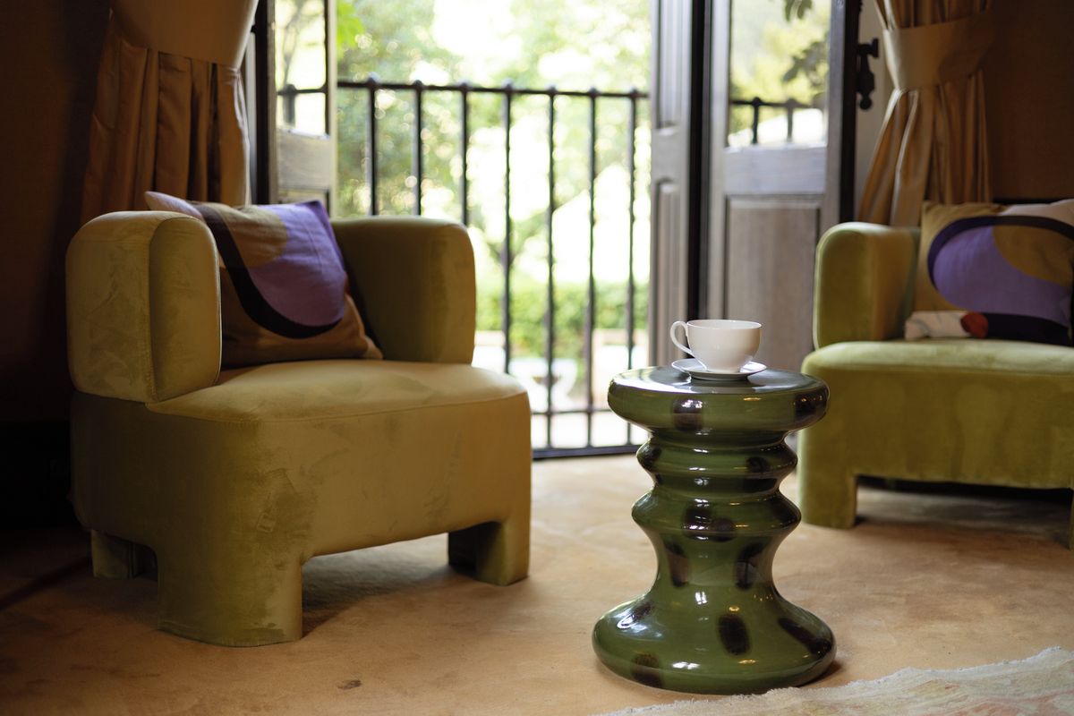 A room with two armchairs, a small table with a cup, and a view through a glass door.