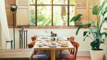 A dining table with chairs, a potted plant, and a window with shutters.