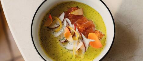 A bowl of food with a green sauce, fish, and garnishes on a white surface.