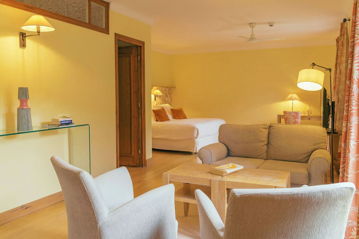 Una habitación de hotel con una cama, un sofá, una mesa de vidrio y un escritorio con una lámpara.