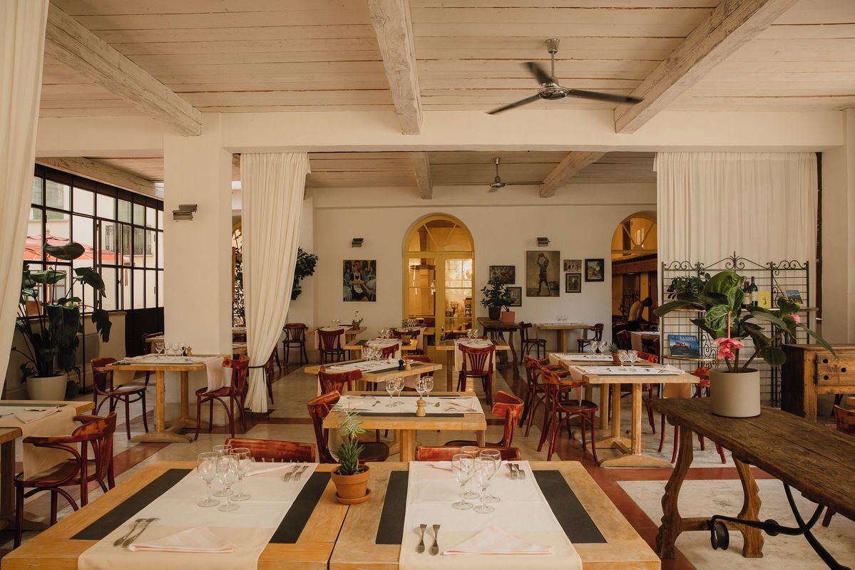 A restaurant with wooden tables and chairs, a ceiling fan, and potted plants.